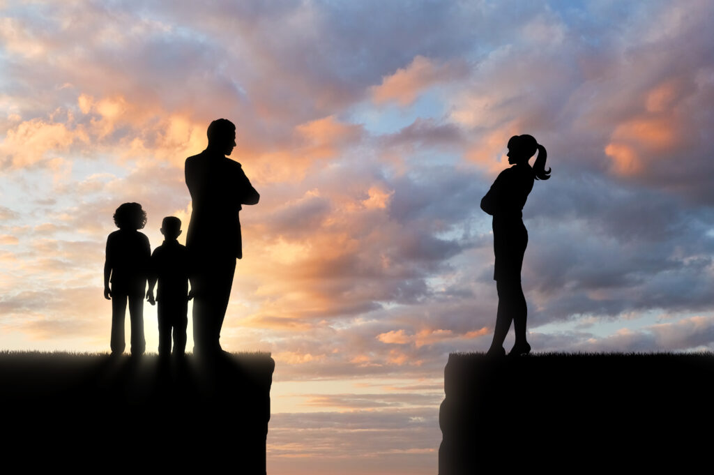 Silhouette of a family divided on separate cliff edges against a sunset sky, depicting the emotional distance and separation involved in a child custody battle during a divorce.